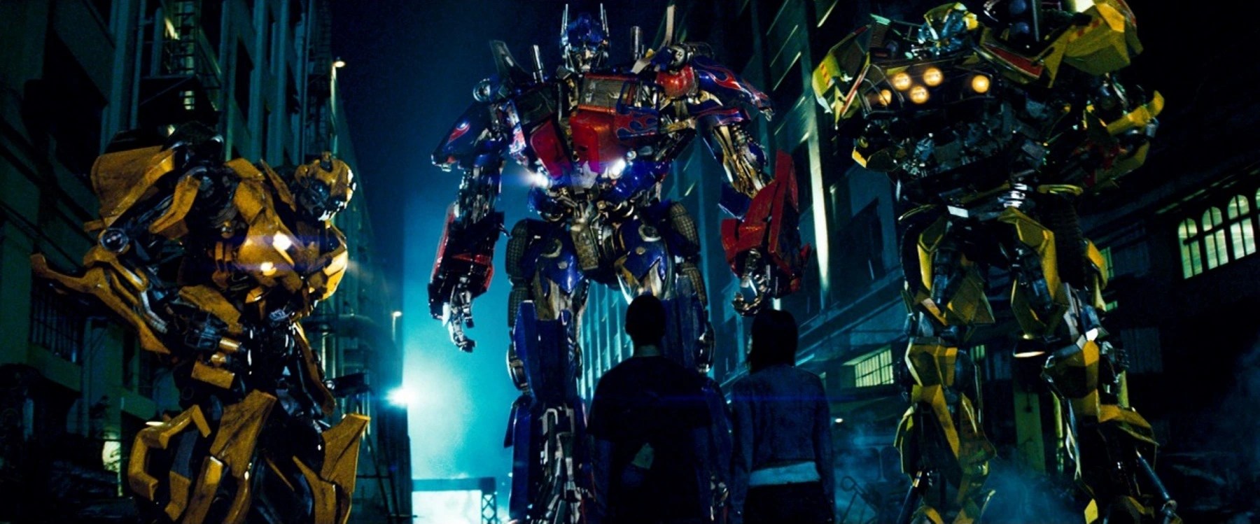 Un trio de grands robots devant un jeune homme et une femme dans une ruelle sombre dans Transformers