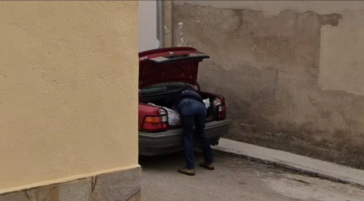 Un homme se penchant sur un paquet de forme humaine dans le coffre d'une voiture