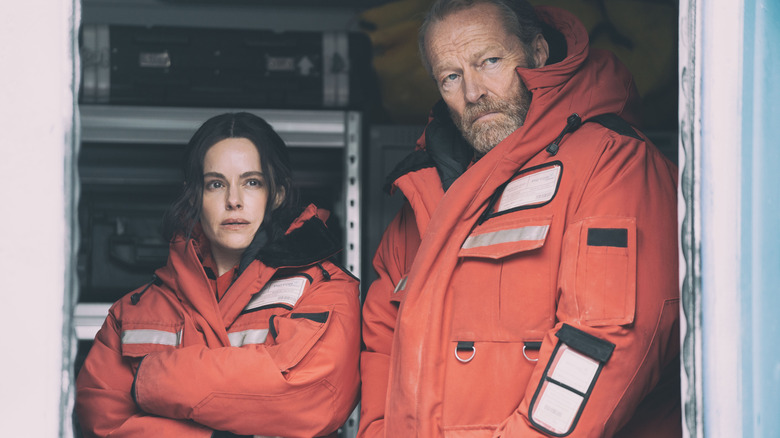 Emily Hampshire et Iain Glen observant à travers une porte dans The Rig