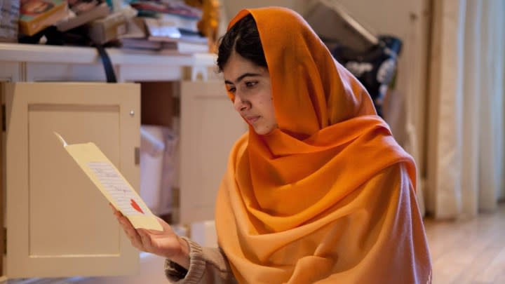 Malala assise par terre en train de regarder un papier dans He Named Me Malala.