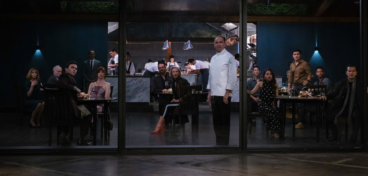 Un groupe de personnes observe à travers les fenêtres du restaurant jusqu'au plafond dans 'The Menu'.