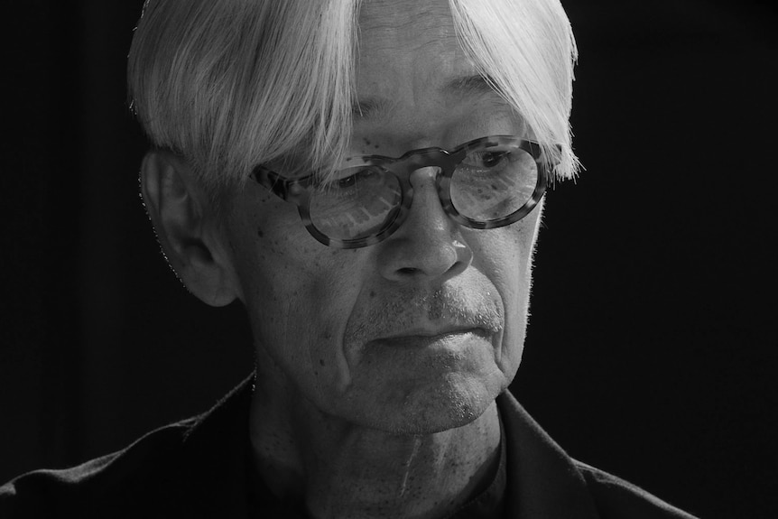 Image en noir et blanc d'un vieil homme japonais avec des lunettes. Il a de longs cheveux blancs.