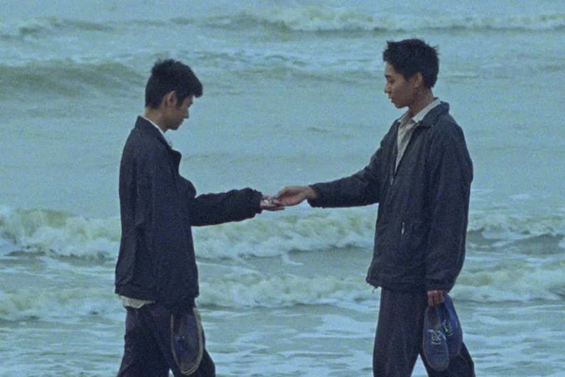 Deux hommes en costume se tiennent dans les vagues d'une plage, main dans la main comme dans une poignée de main.