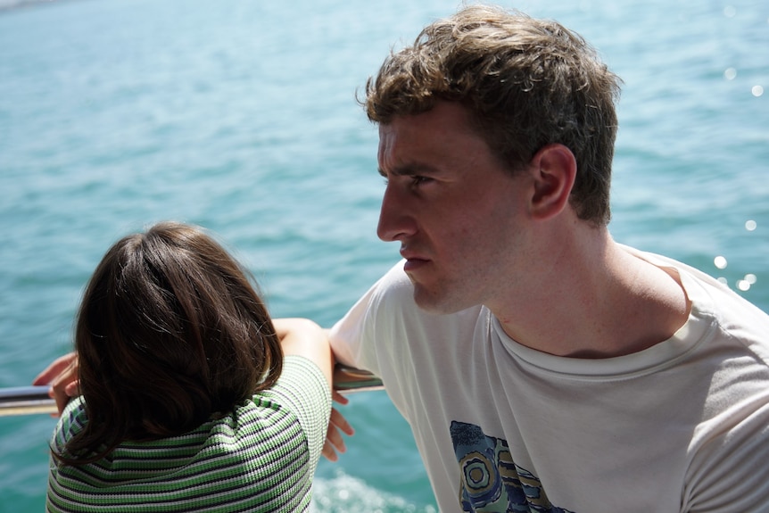 Une jeune fille fait face à l'eau, et un homme dans la fin de sa vingtaine est assis sur un bateau.