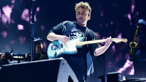 Sam Fender sur scène, tenant une guitare électrique bleu clair