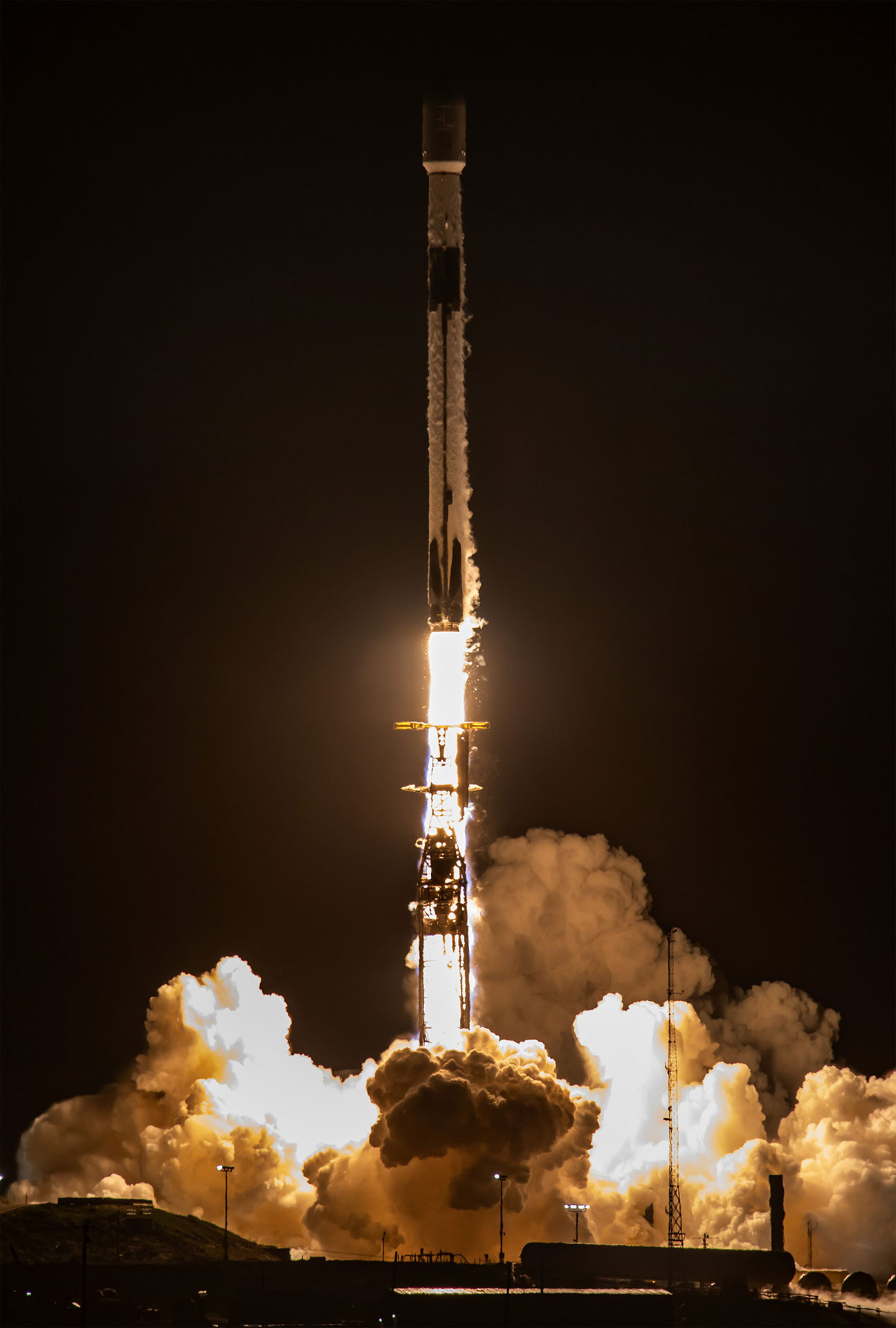 Un fusée Falcon 9 de SpaceX s'élève dans le ciel nocturne, son moteur émettant une lueur orange-blanche illumine sa rampe de lancement.