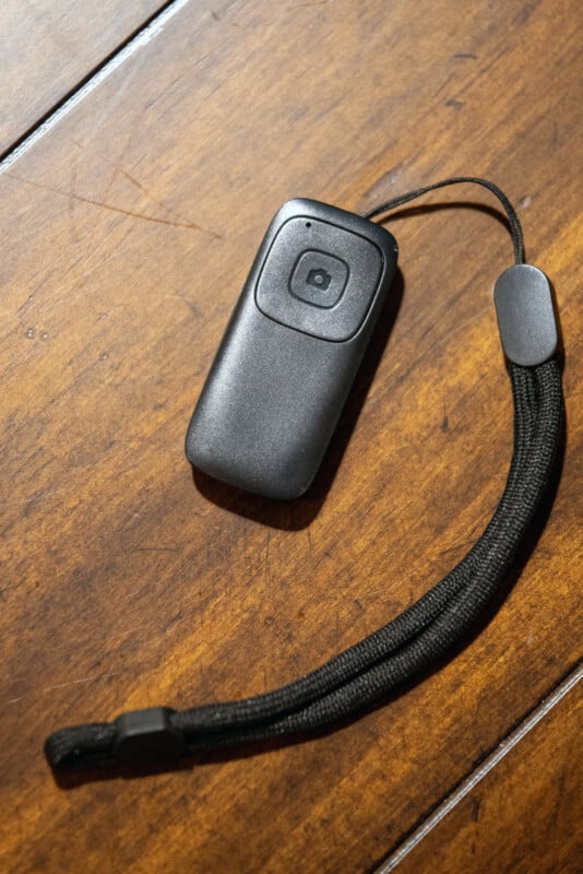 Un petit appareil électronique noir avec un bouton unique et une dragonne étant posé sur une surface en bois.