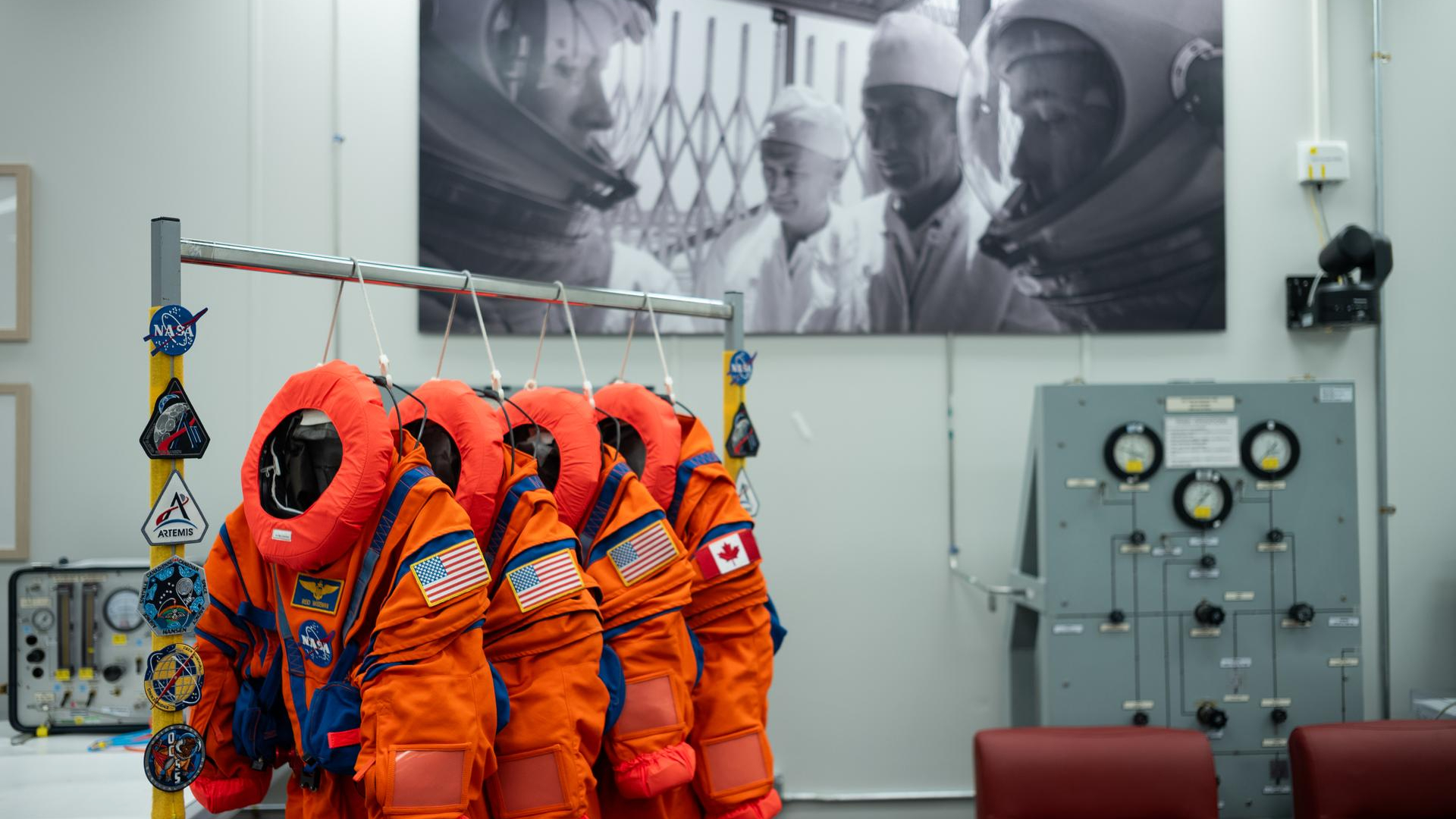 Quatre combinaisons spatiales orange brillante avec le logo circulaire de la NASA suspendues sur un support dans une pièce vide