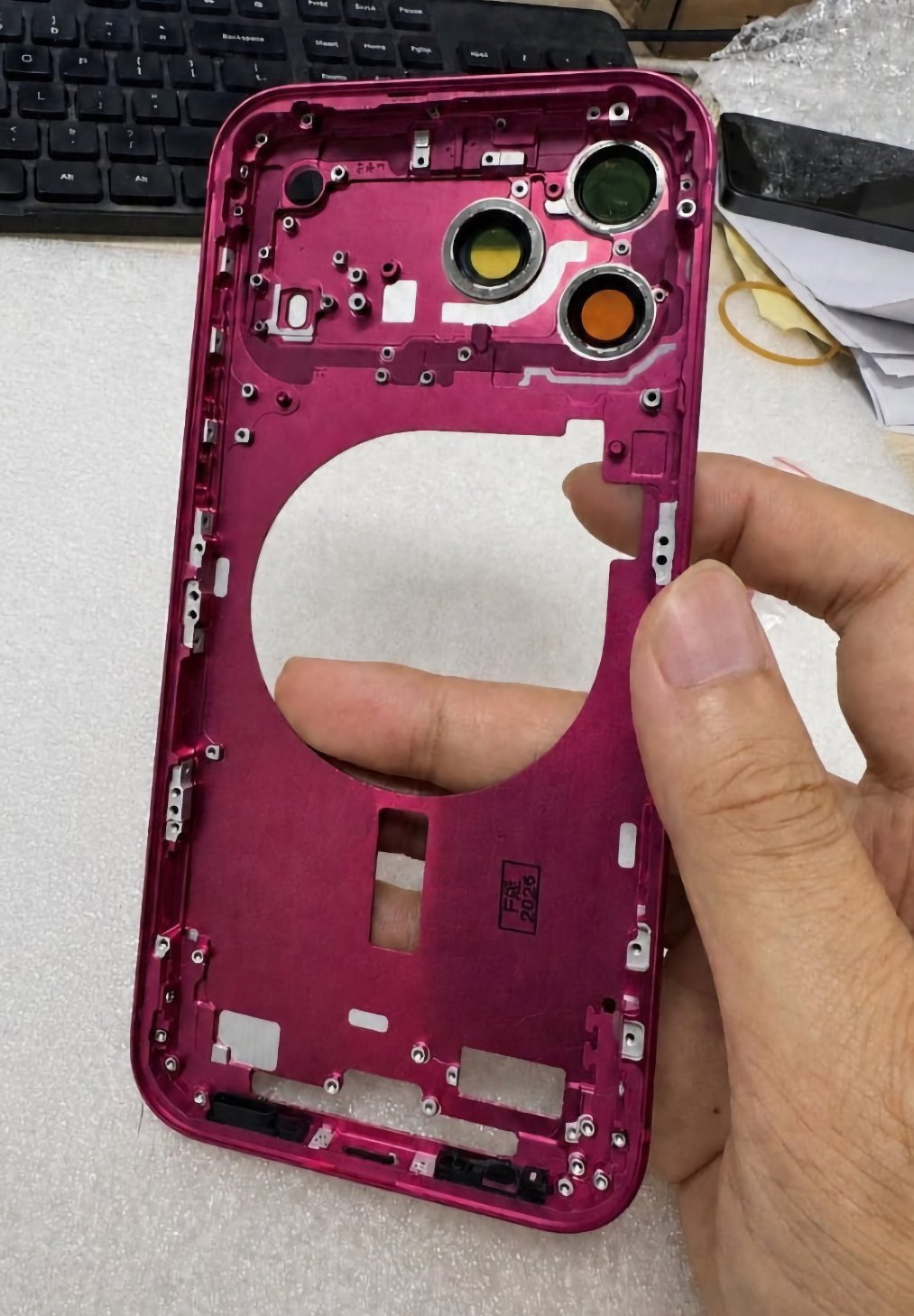 Un cadre de smartphone métallique magenta, avec un large ouverture circulaire et trois espaces pour objectifs, posé sur une surface claire