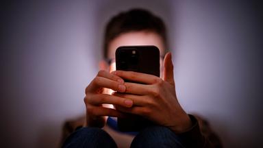 Un jeune utilise son smartphone dans une pièce sombre.
