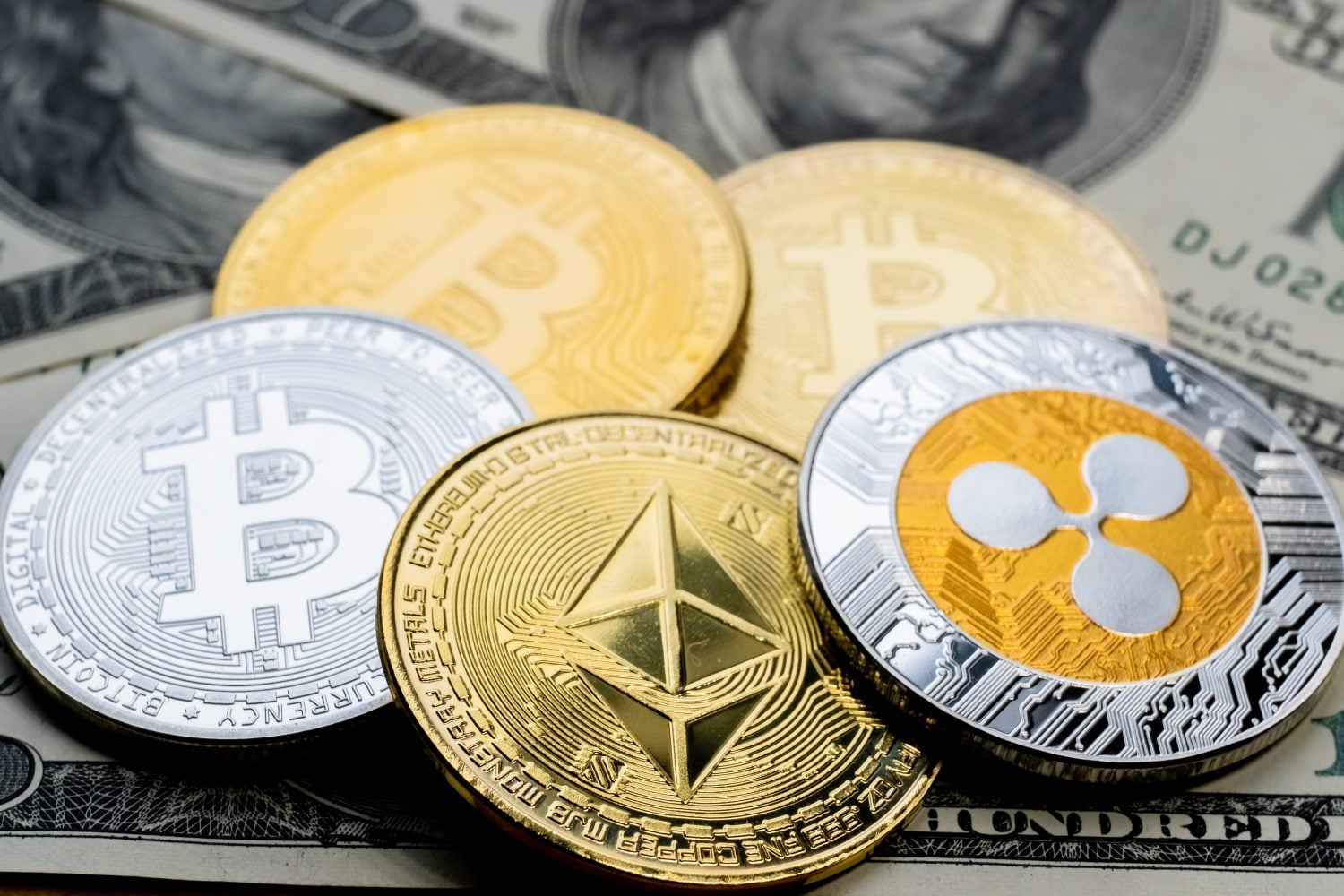 Pièces de crypto-monnaie Bitcoin, Ethereum et Ripple sur des billets de 100 dollars américains