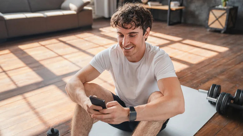 Personne assise par terre après une séance d'entraînement, regardant son téléphone.
