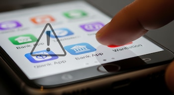 Écran de téléphone avec des icônes d'applications bancaires, un doigt touchant l'écran et un symbole d'avertissement triangulaire.
