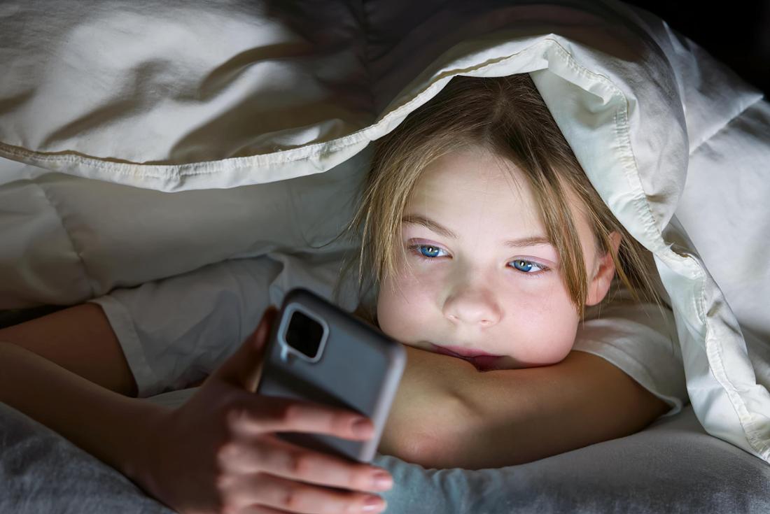Une jeune fille sous une couverture utilisant son téléphone