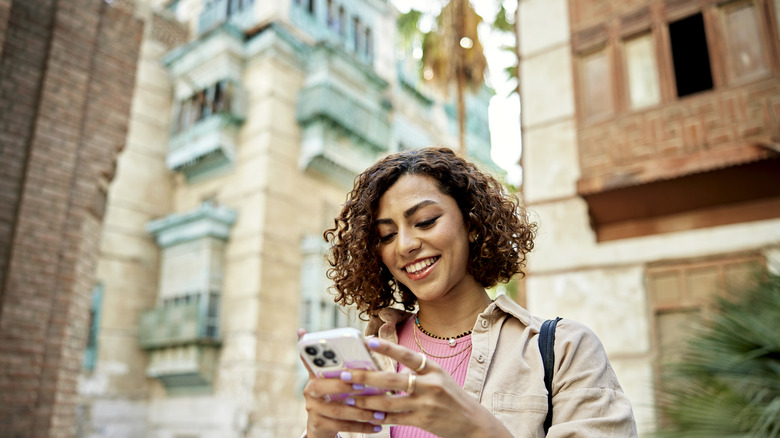 Une femme sourit en tenant son smartphone.