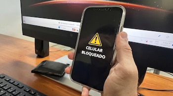 Une main tenant un téléphone mobile avec le message 'cellulaire bloqué' sur un écran.