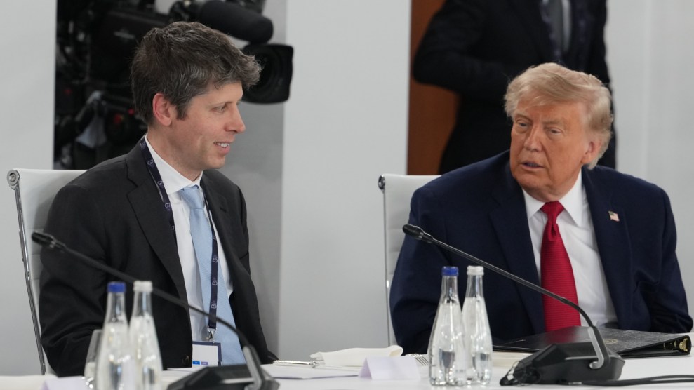 Donald Trump (droite) et Sam Altman (gauche) discutent ensemble. Ils portent des costumes et sont assis à une table blanche avec des microphones.