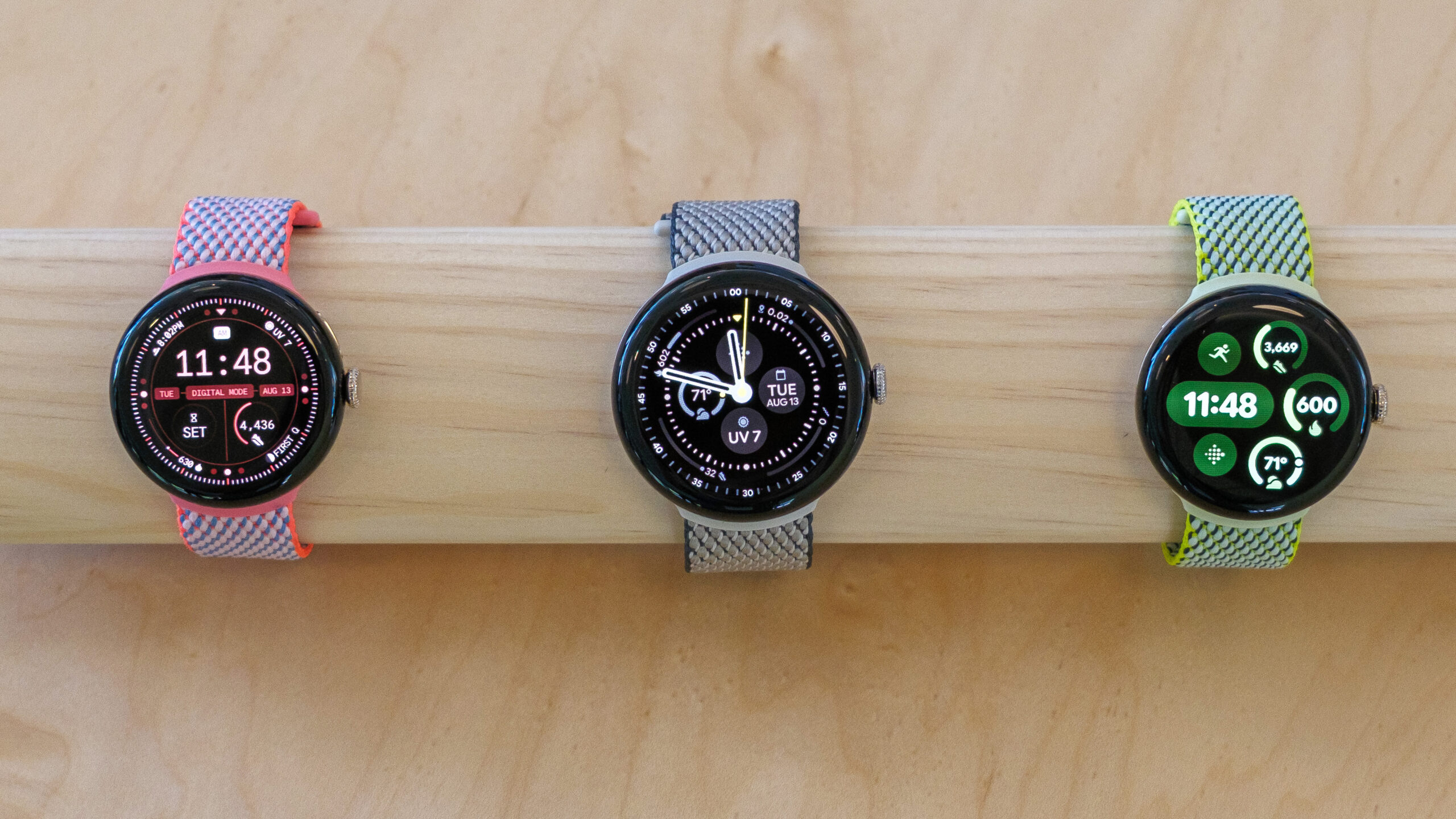 Trois modèles de Google Pixel Watch 3 sur une étagère en bois.