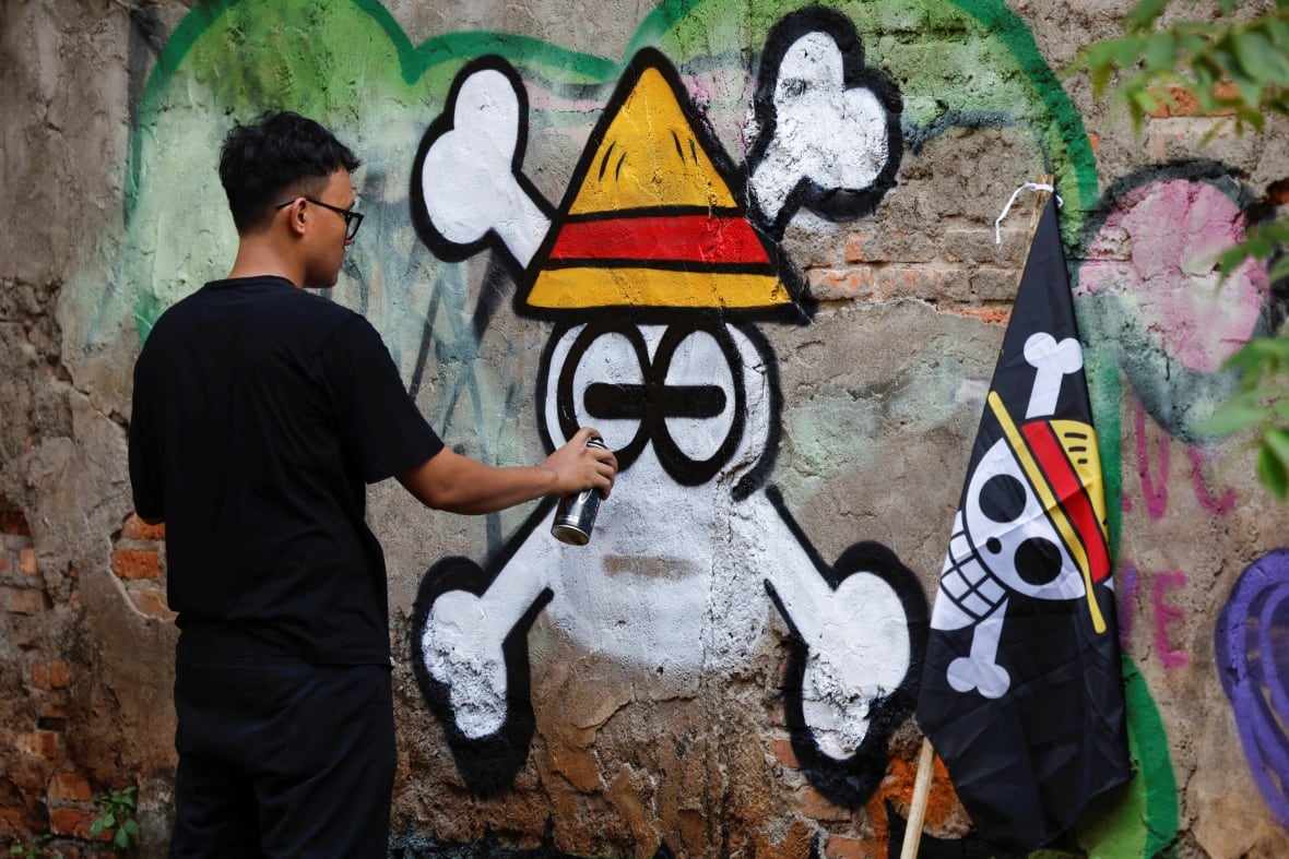 Un individu peint un mur avec un crâne portant un chapeau triangulaire jaune.