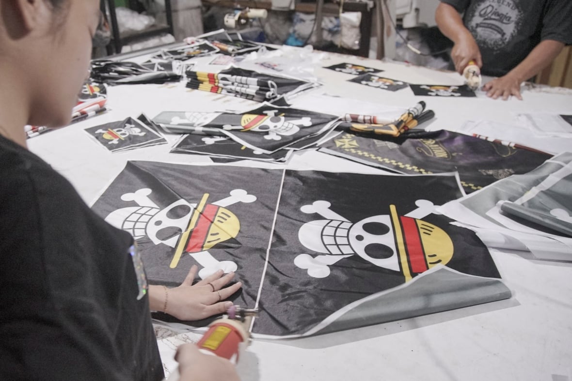 Un individu découpe des drapeaux noirs représentant un crâne portant un chapeau de paille.