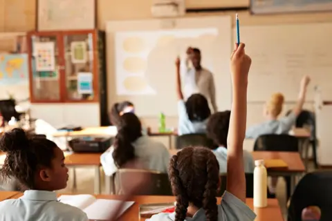 Des élèves dans une salle de classe avec plusieurs mains levées.