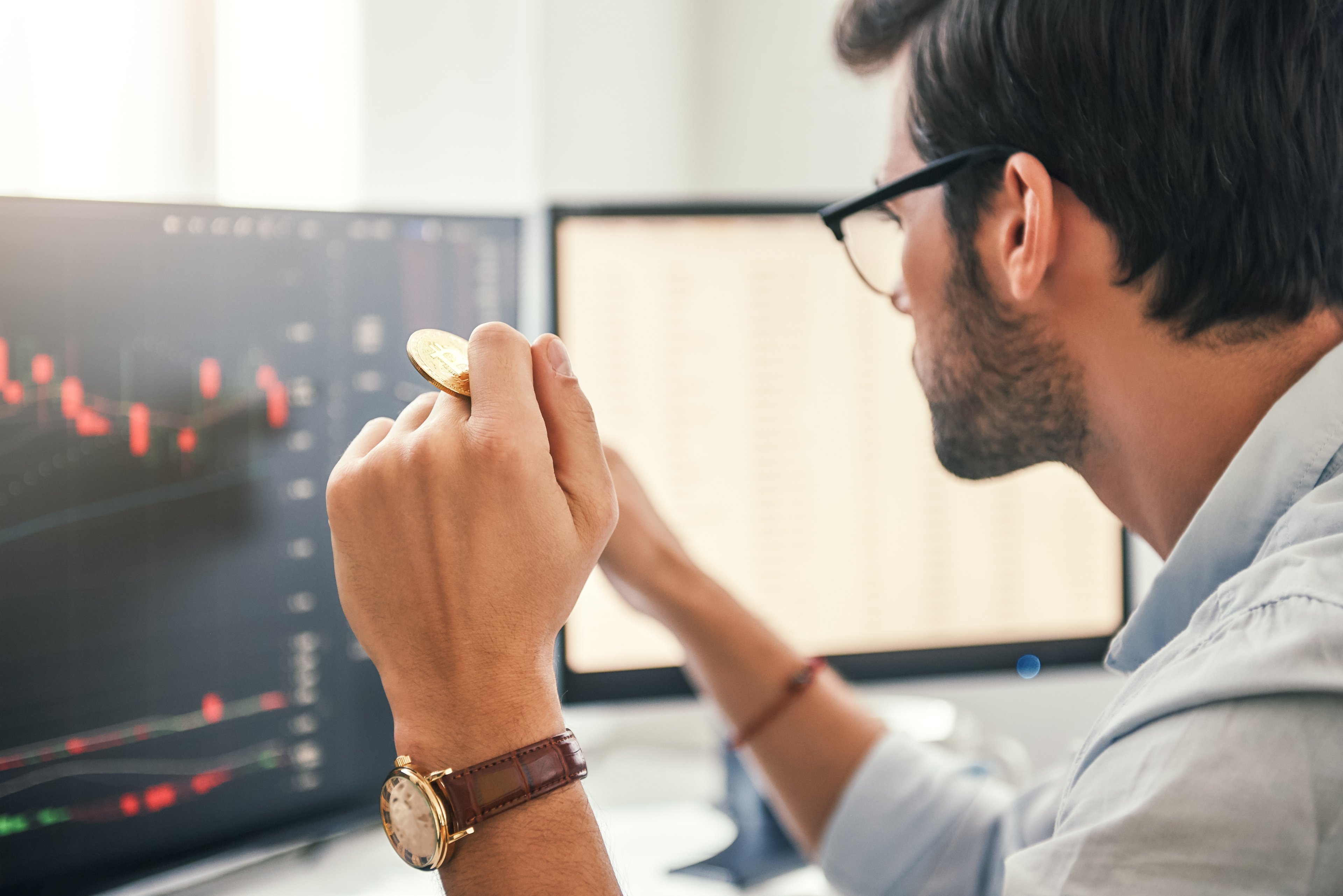 Investisseur observant des cryptomonnaies depuis son ordinateur, tenant une pièce en or.