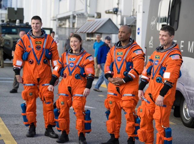 Quatre astronautes en tenues orange, trois hommes et une femme.