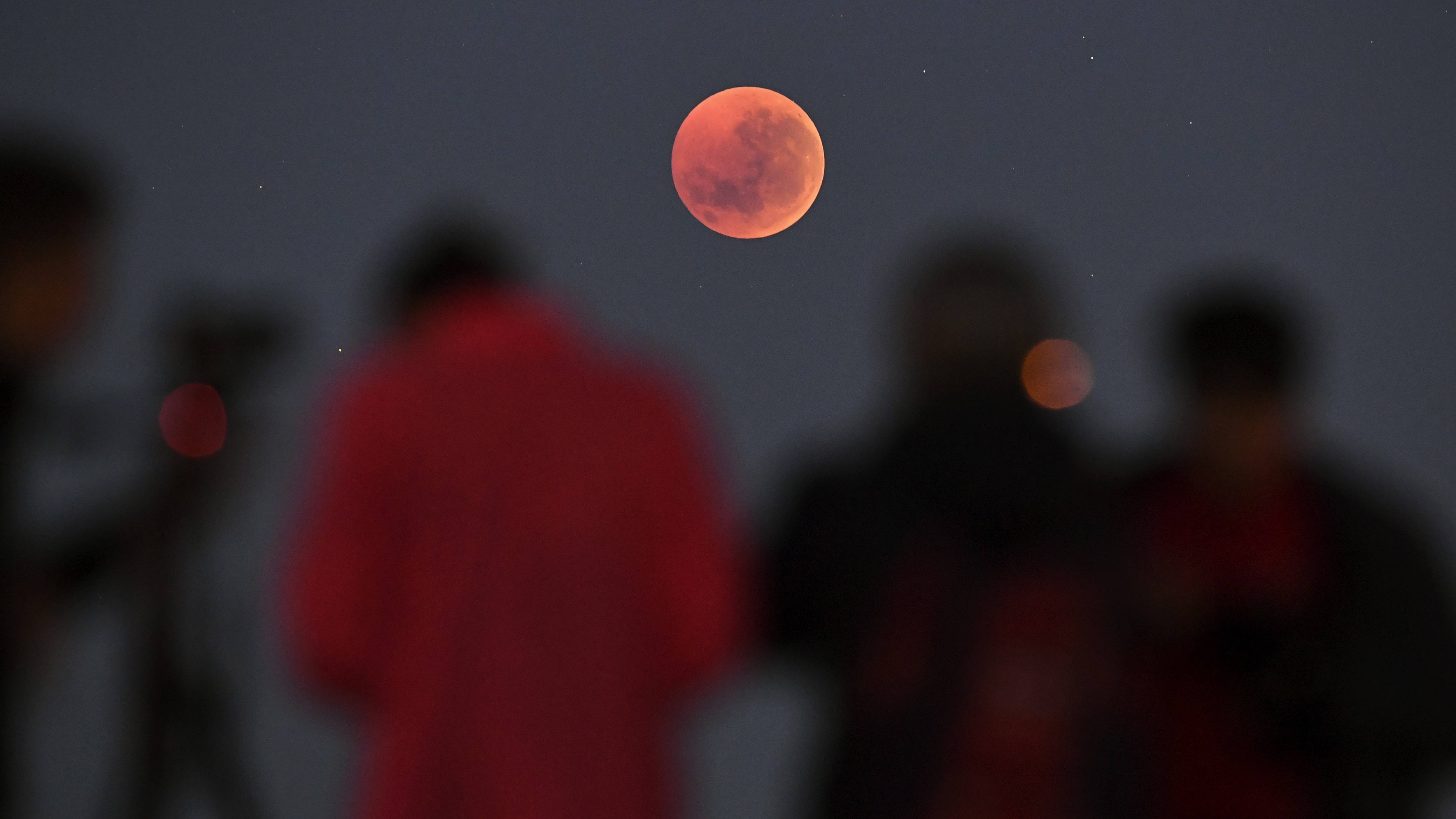 des gens se tiennent et regardent une éclipse lunaire totale de lune de sang dans le ciel.