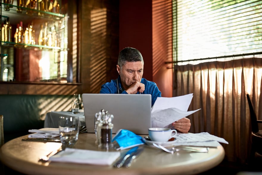 Un investisseur assis à un café examinant un dossier à côté d'un ordinateur portable.