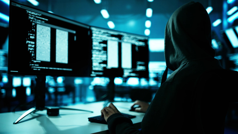 Hacker encapuchonné devant deux écrans affichant du code