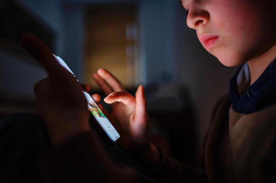 Un jeune dans une chambre sombre avec son téléphone