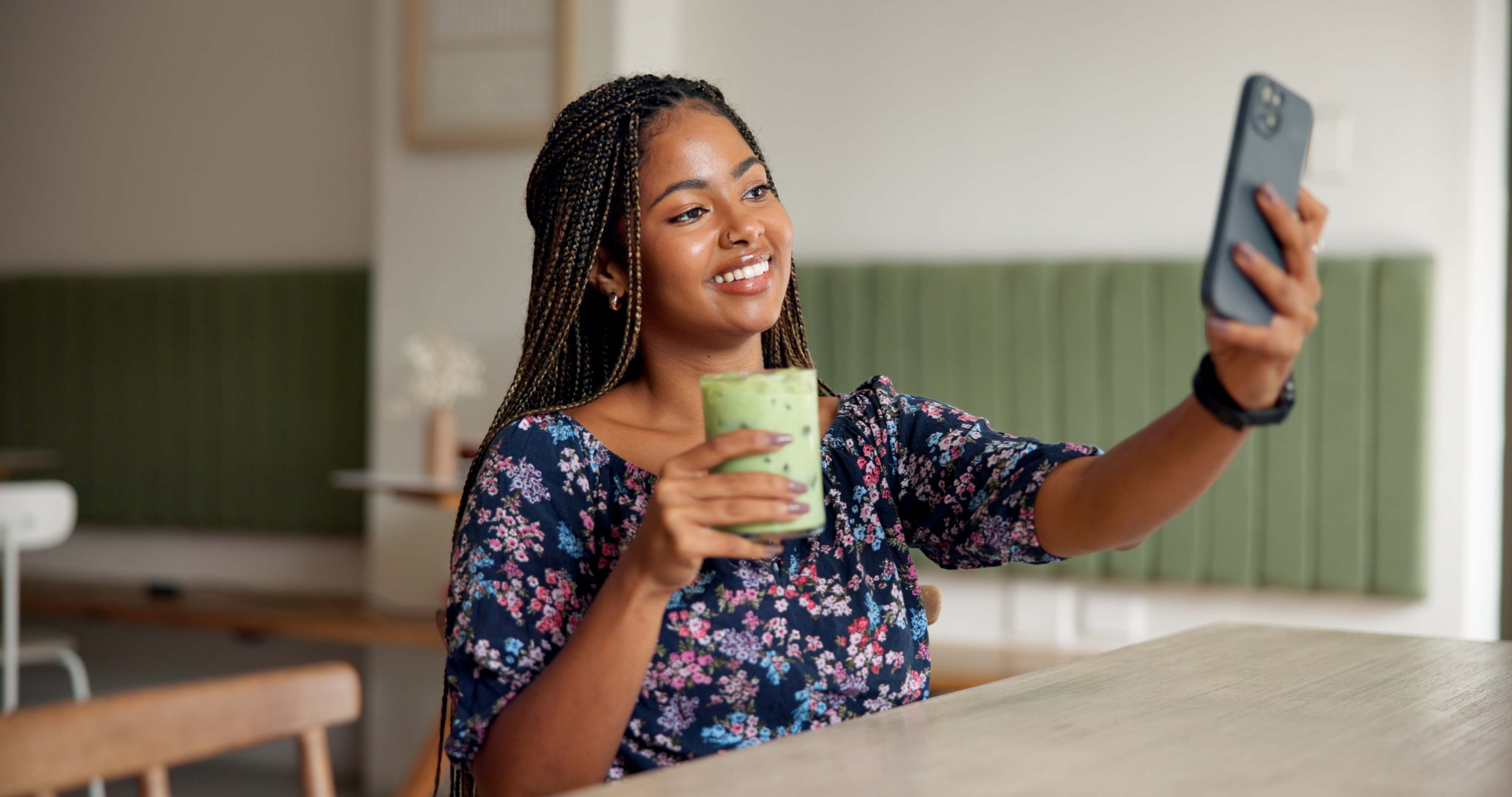Une femme heureuse se prend en selfie avec son jus vert dans un café, illustrant une publication pour les réseaux sociaux.