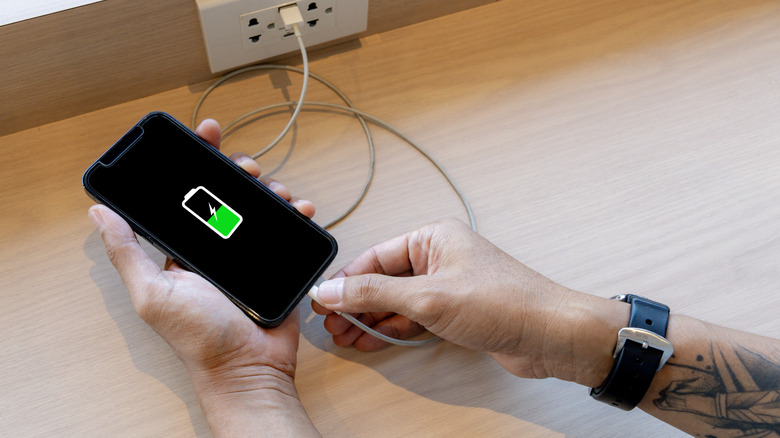 Main tenant un téléphone branché à un chargeur avec une icône de batterie visible à l'écran.