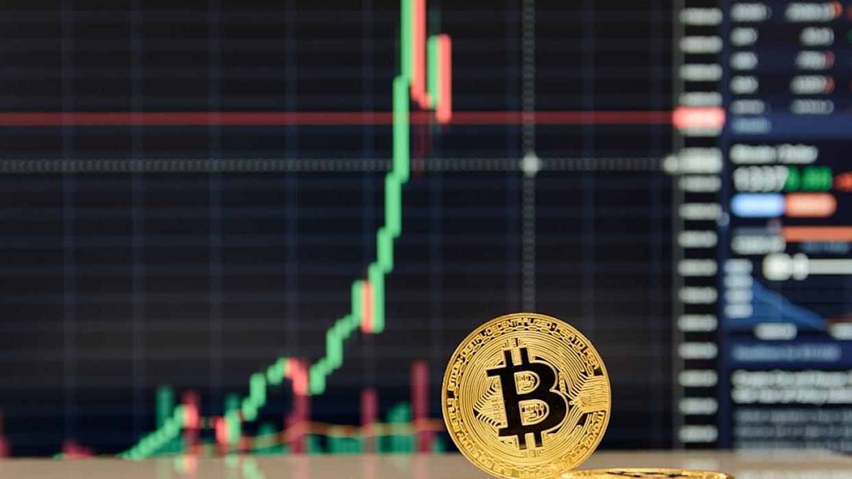 Un bitcoin doré devant des graphiques boursiers.
